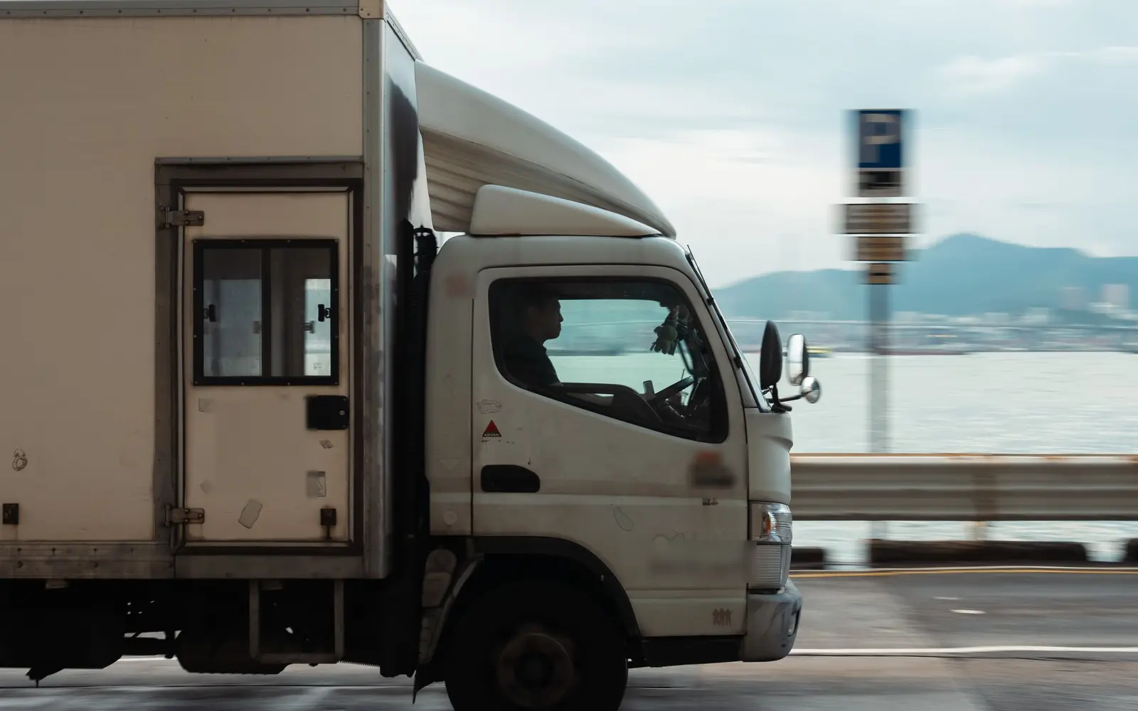 海沿いの道を走るトラックと運転席のドライバー